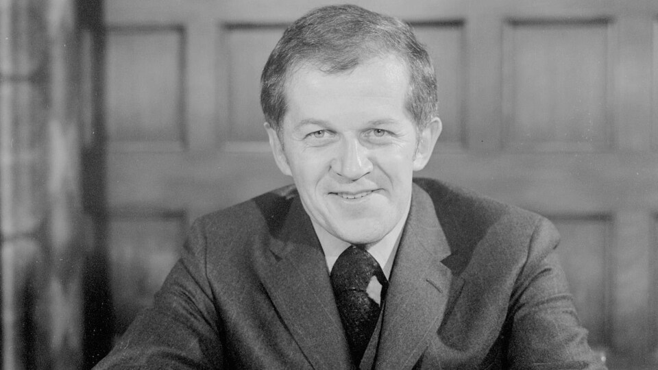 Gérard Lebel, souriant et assis à un bureau lors d'une séance de photographie officielle.