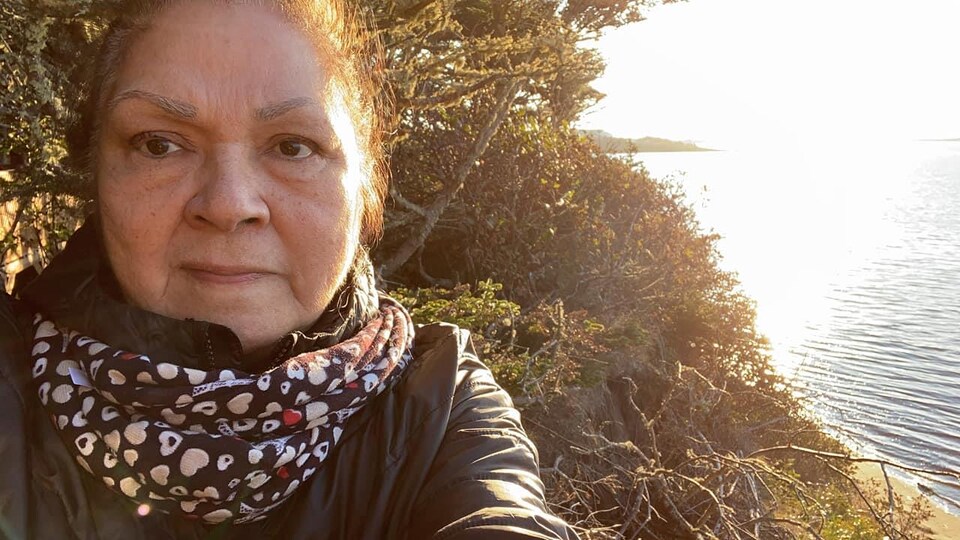 Germaine Mckenzie se tient debout devant la mer, des arbres et des arbustes.