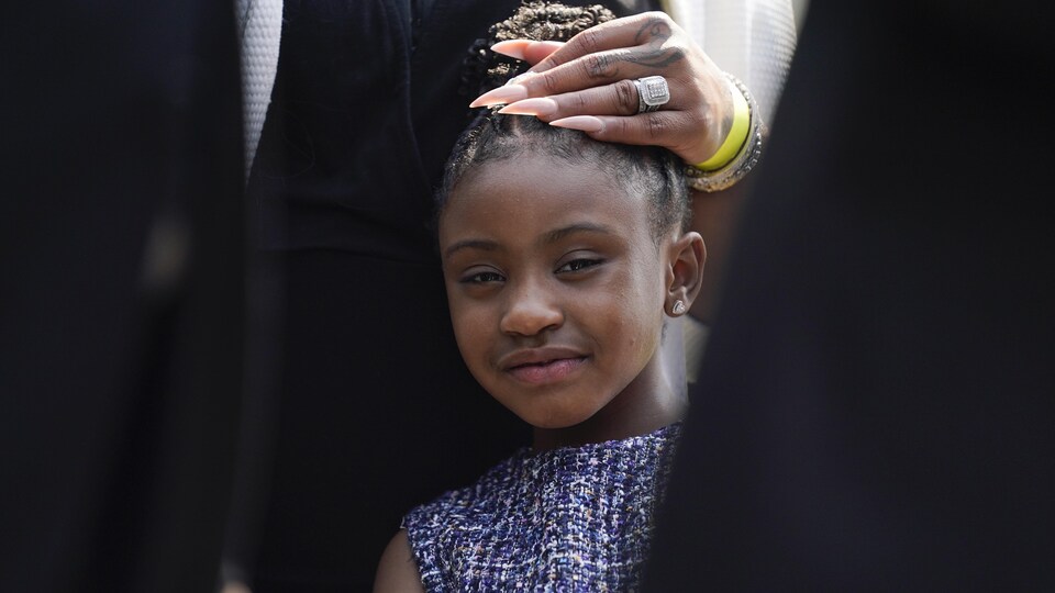 Une femme aux ongles très longs, a la main sur la tête de Gianna Floyd, qui a les cheveux attachés.