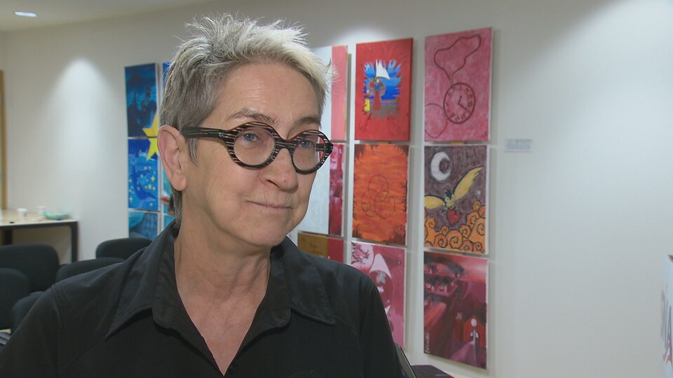 Carmen Gibbs en entrevue devant des tableaux qui évoquent le drapeau acadien.