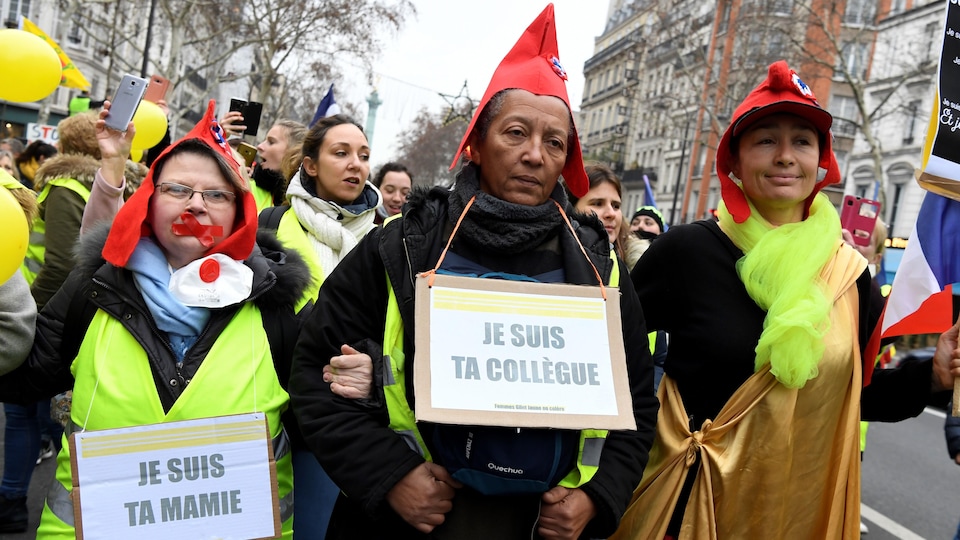 Trois femmes se tiennent par les bras en marchant. Elles portent un bonnet phrygien.