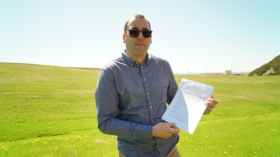 Photographié devant un champ verdoyant des Îles, il montre les pétitions en question.