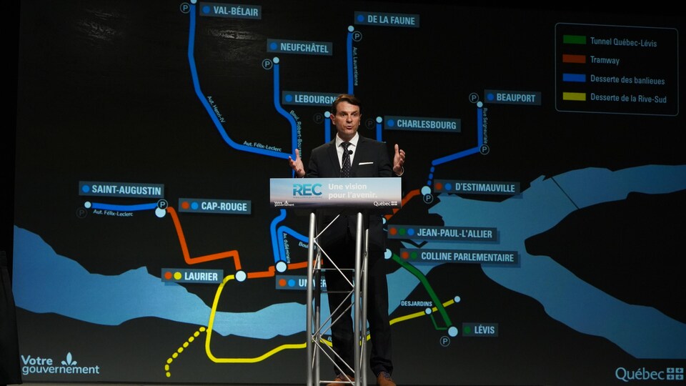François Bonnardel derrière le podium lors de la conférence de presse avec la carte du Réseau express de la Capitale en arrière-plan. (archives)