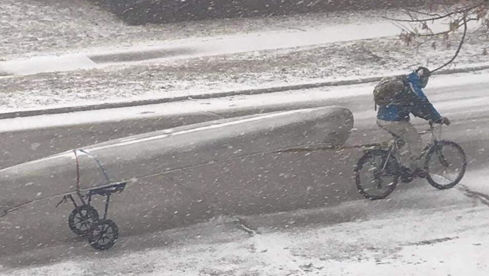 Un homme à bicyclette remorque un canot en pleine tempête de neige