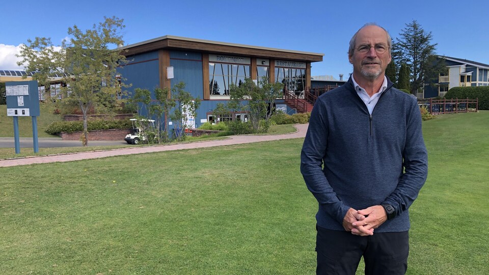 Un homme pose devant le bâtiment d'accueil du club de golf.