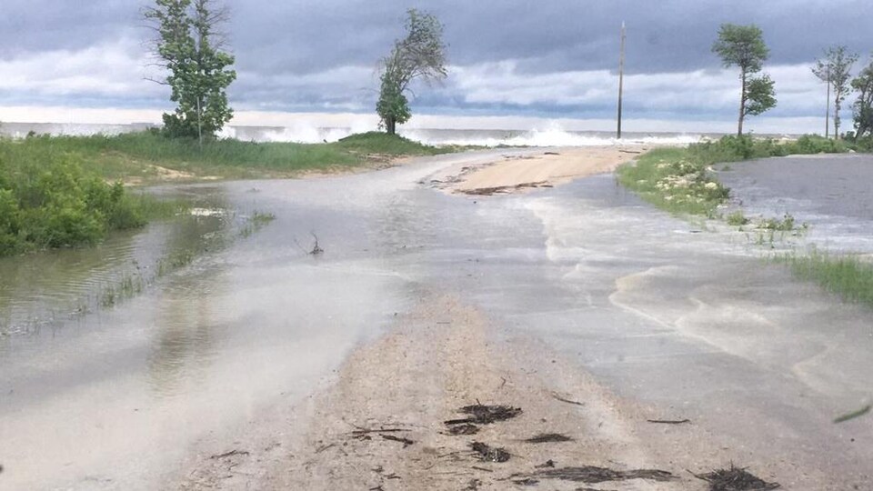 De l'eau se déverse sur une route qui mène à la plage de Willow Island, où frappent de hautes vagues du lac Winnipeg, le 26 juin 2022.