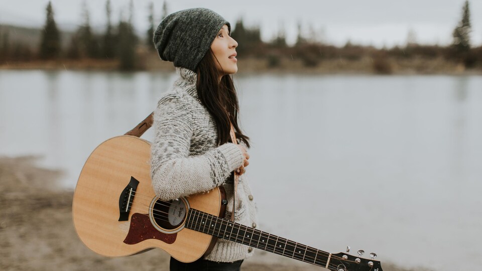 La chanteuse Ginalina tenant sa guitare près d'un lac en hiver.