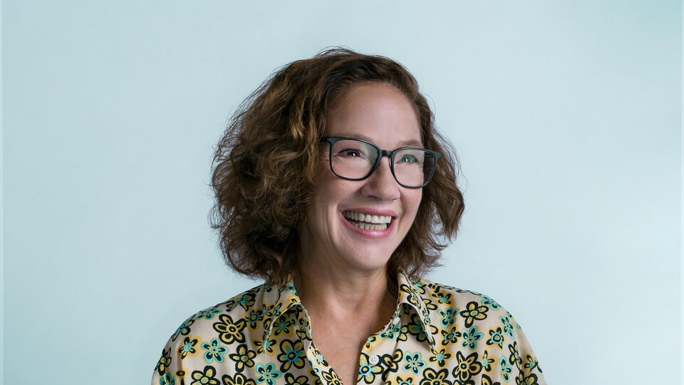 Portrait de la femme tout sourire devant un fond bleu pâle.