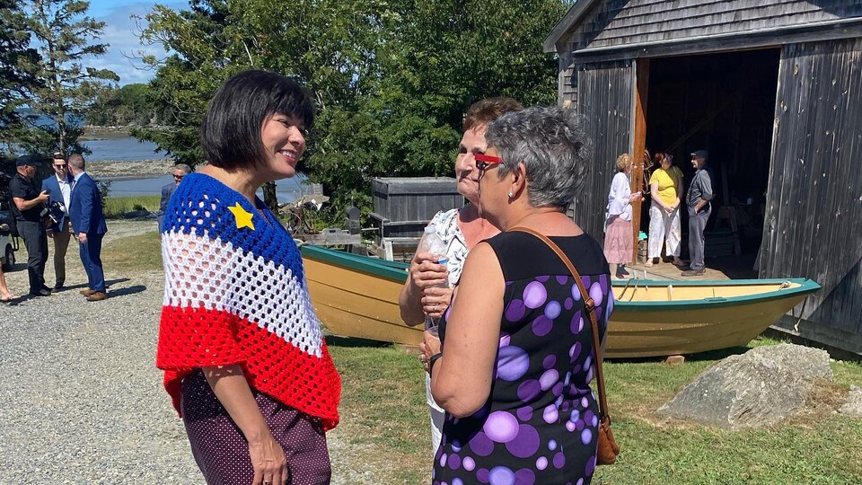 La ministre porte un châle au couleur du drapeau acadien et parle avec des gens de la région.