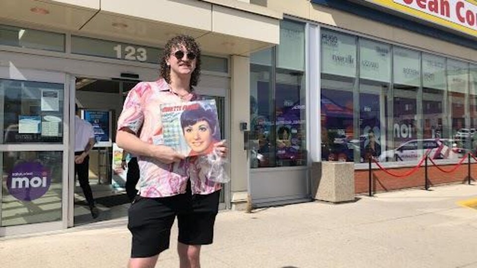 un homme tient un disque vynile devant un magasin Jean-Coutu