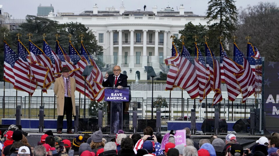 Rudy Giuliani s'adresse à une foule de supporters de Donald Trump. Il est debout devant un podium sur lequel est inscrit « Sauvons l'Amérique ». On voit la Maison-Blanche derrière lui.