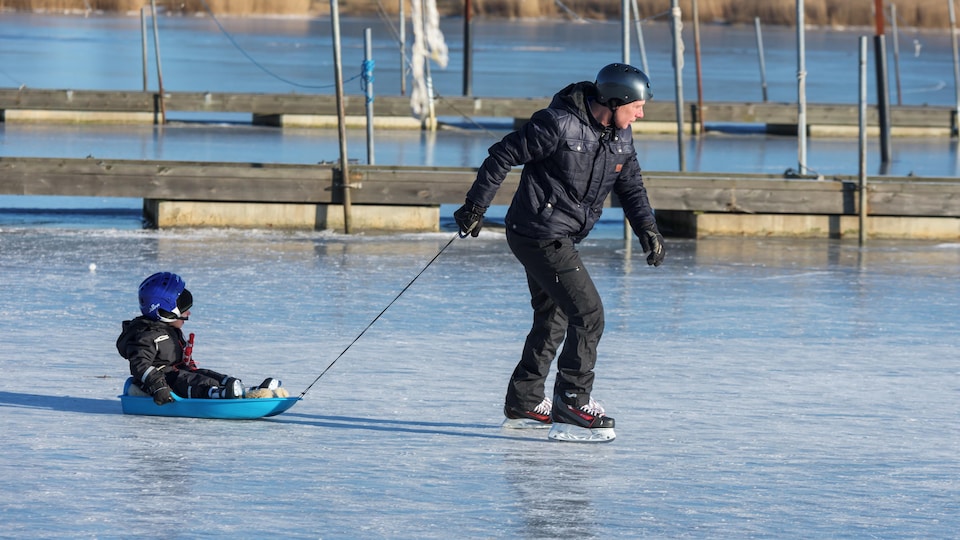 Un homme en patins tire un enfant dans un traîneau sur la glace.