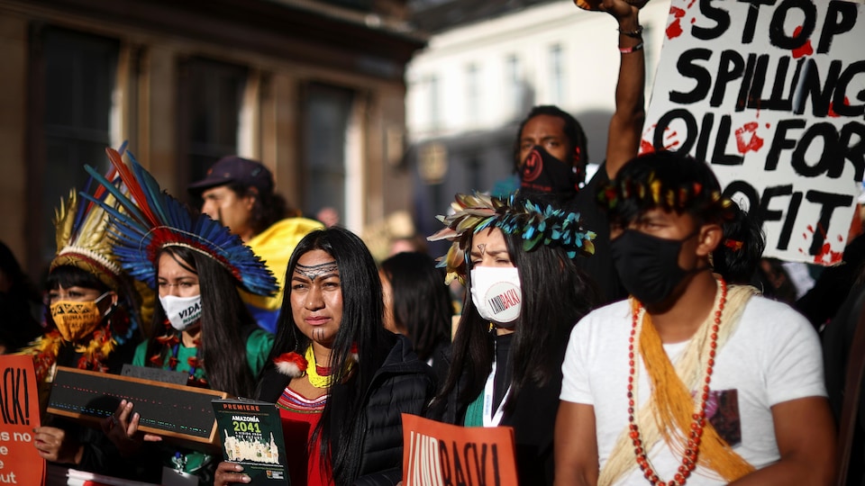 Des Autochtones portant des coiffes traditionnelles tiennent des pancartes dans une foule.