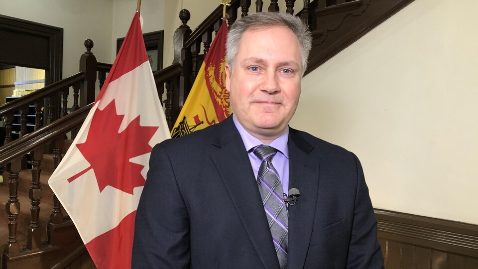 Le député de Saint-Jean-Est, Glen Savoie, après son assermentation à titre de ministre de la Francophonie dans la résidence du gouverneur. Il pose devant les drapeaux du Canada et du Nouveau-Brunswick.