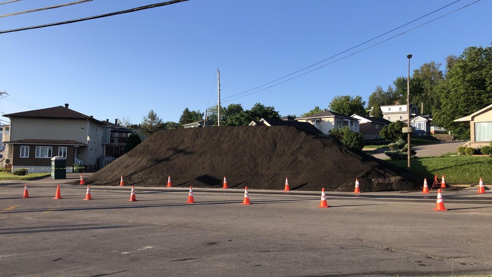 Un amoncellement de terre au coin d'une rue et des cônes orange.