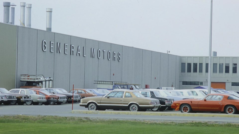 Devanture de l'usine General Motors et voitures stationnées. 