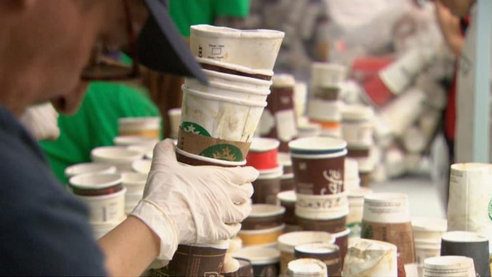 Une main gantée tient une pile de contenants en carton et on vous aussi plusieurs contenants similaires empilés en arrière-plan