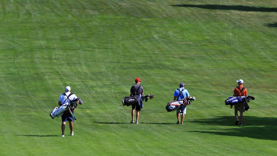 Quatre hommes marchent sur un terrain de golf avec leur sac en bandoulière.