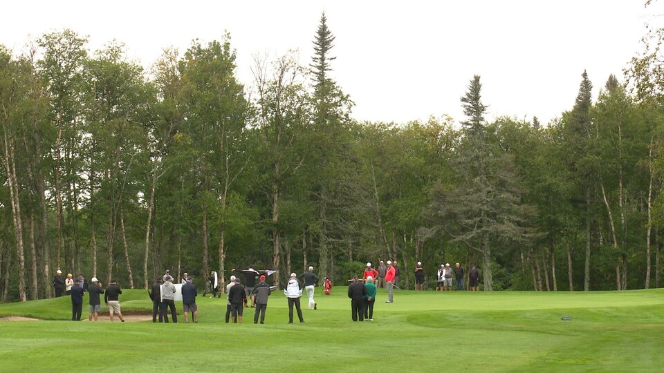 Une trentaine de spectateurs regarde des golfeurs à l'oeuvre