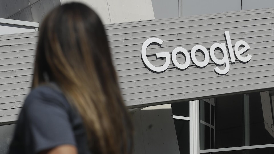 Une femme marche devant un immeuble avec une enseigne de Google sur la façade