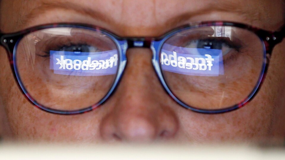 Le reflet du logo de Facebook sur les lunettes d'une femme.