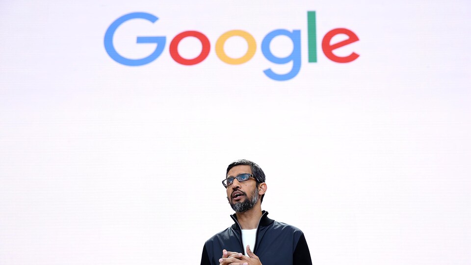 Le PDG de Google, Sundai Pichar, se tient devant un écran blanc sur lequel est inscrit "Google". 