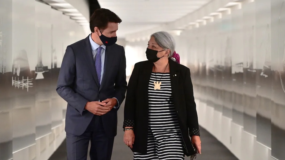 M. Trudeau et Mme Simon, tous les deux masqués, marchent côte à côte dans un corridor.