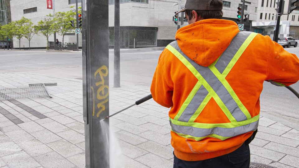 Un employé efface un graffiti sur une colonne.