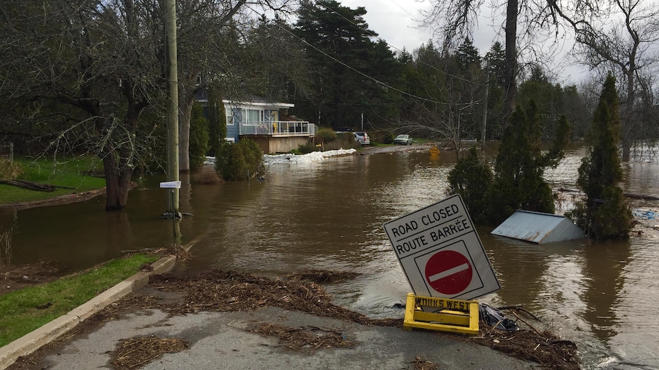 Une route inondée et fermée à la circulation. L'inondation s'approche d'une maison entourée de sacs de sable.