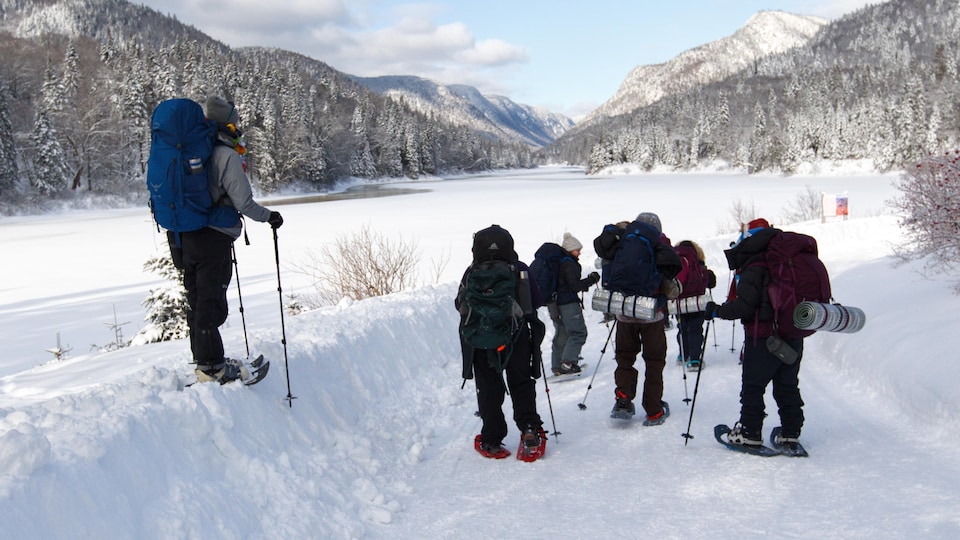 Les jeunes marchent avec des raquettes dans un sentier enneigé. On voit des montagnes au loin.