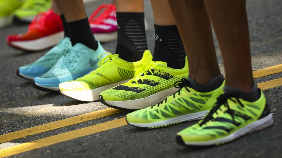Gros plan sur les pieds de trois athlètes, chaussés par des souliers de course aux couleurs vives.