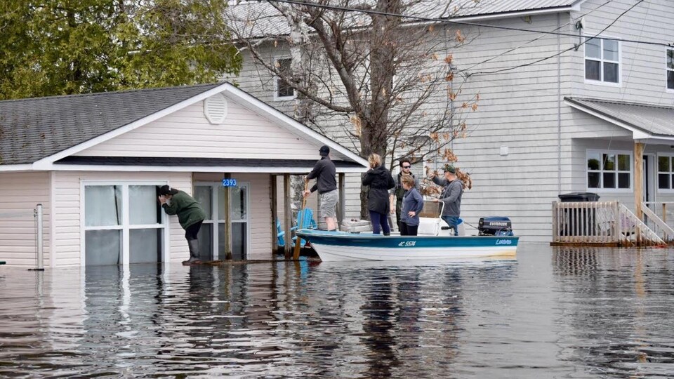 Des gens sur un canot près d'une maison inondée vérifient s'il y a toujours quelqu'un à l'intérieur.