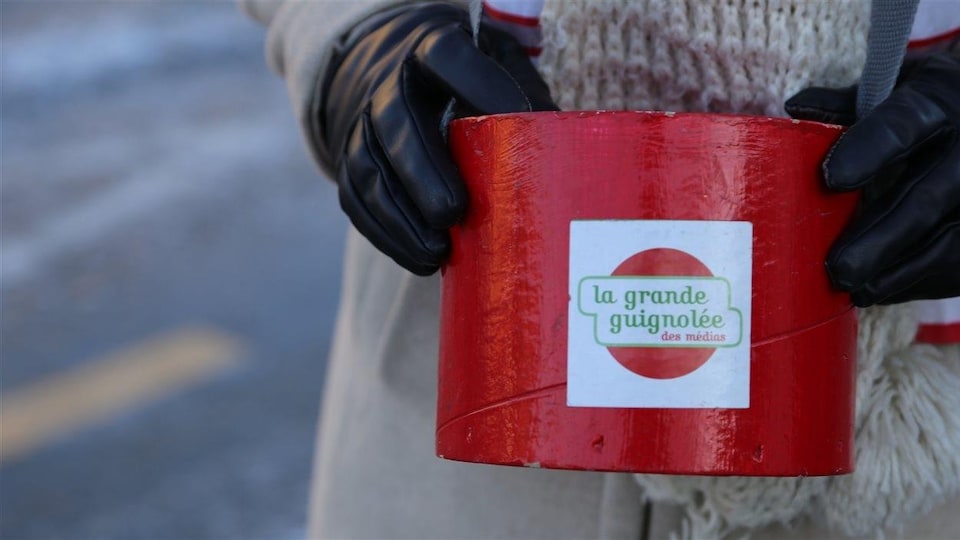 Une personne tient dans ses mains une boîte rouge pour recueillir des dons. 