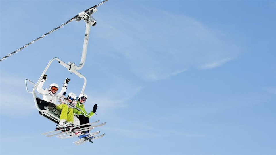 Une famille au ski. Ils sont assis dans un télésiège.