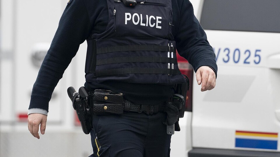 Plan rapproché du gilet pare-balles que porte un membre de la GRC. Le vêtement est noir avec le mot « Police » écrit en lettres blanches.