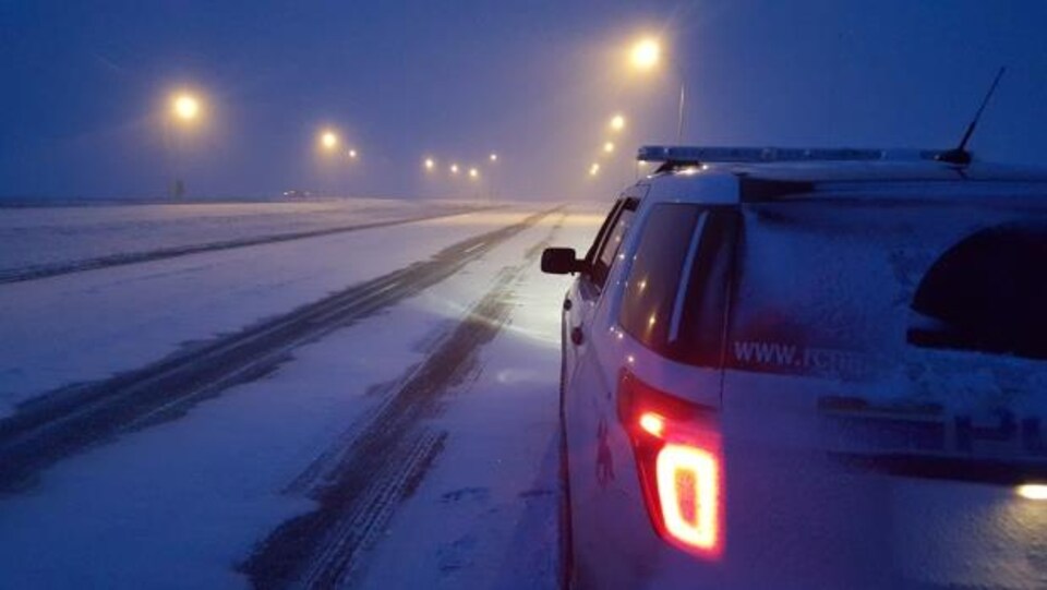 Une voiture de la GRC sur une route enneigée la nuit.