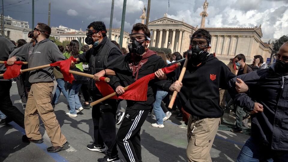 Des hommes masqués et armés de bâtons marchent dans les rues d'Athènes, en Grèce.