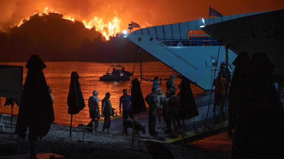 İnsanlar tekneye binerken gece yakındaki ateşlerle aydınlatılıyor.