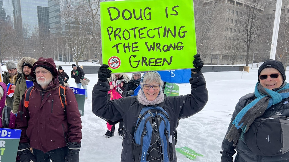 Une femme soulève une pancarte verte pour montrer son opposition au développement urbain de Doug Ford dans la ceinture de verdure.