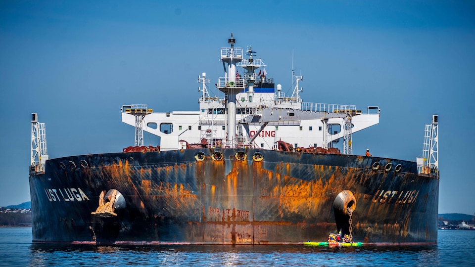 A zodiac aboard with many people can be seen in front of a large tanker. 