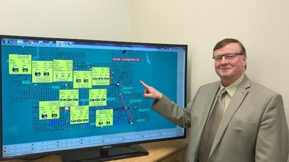 Greg Archibald, dans un bureau, montre un téléviseur sur lequel est affichée une carte.
