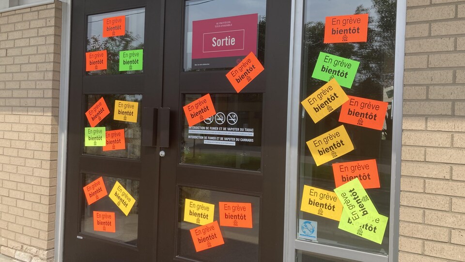 Des affiches sur lesquelles il est écrit « En grève bientôt » sont placardées sur une porte extérieure.