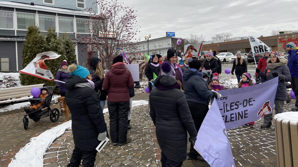 Travailleuses et parents agitent drapeaux et banderole.