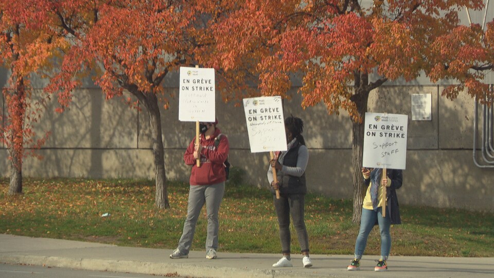 Des employés de l'Université d'Ottawa, en grève, agitent des pancartes.