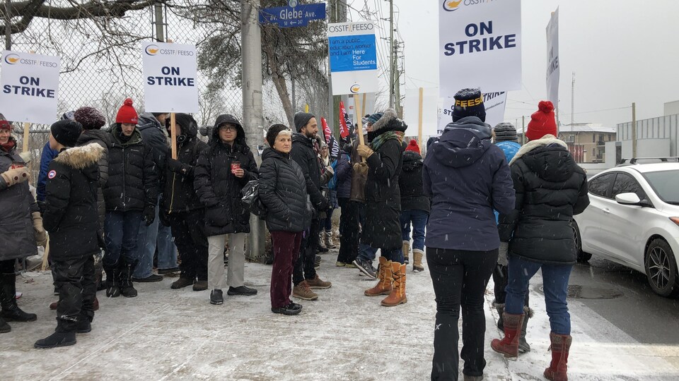Des manifestants sur le coin d'une rue d'Ottawa avec des pancartes en hiver.