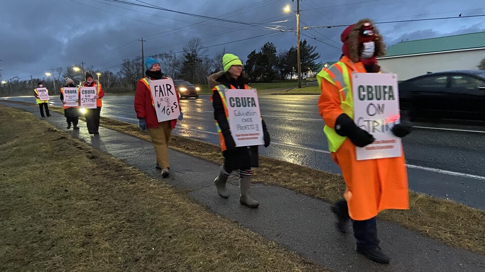 Une demi-douzaine de personnes marchent le long d'une rue en tenant des pancartes syndicales.