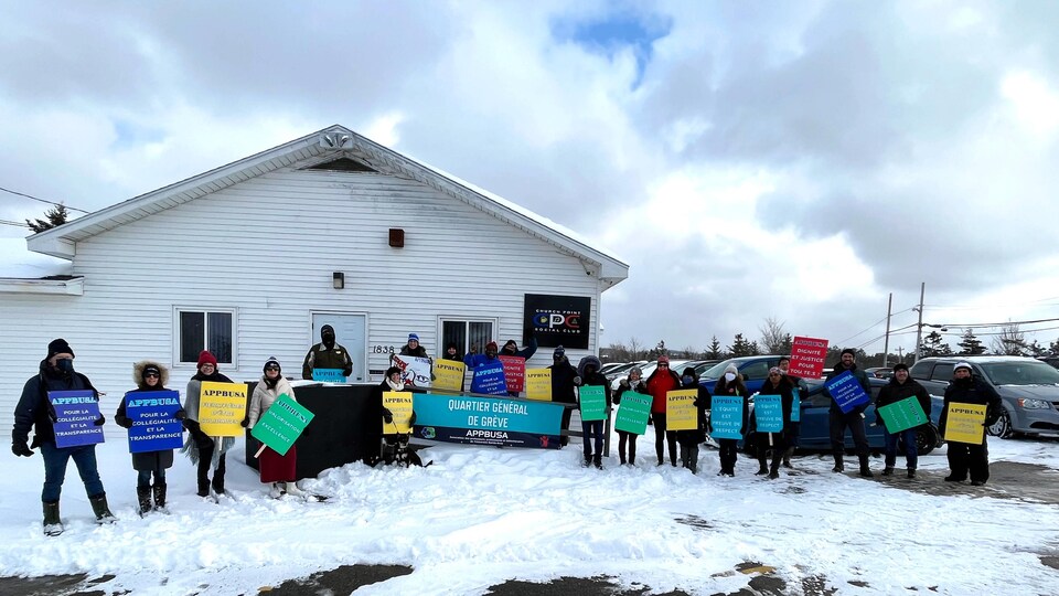 Une vingtaine de personnes en grève, debout dans la neige avec leurs pancartes, posent pour une photo de groupe.