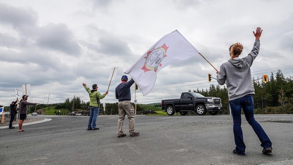 Cinq travailleurs en grève de la minière Vale font des signes aux automobilistes qui roulent devant leurs piquets de faire du bruit avec leur klaxon.