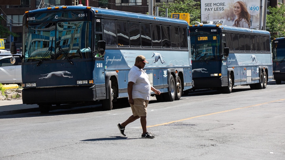 Un homme traverse la rue devant des autocars de Greyhound stationnés près du terminus de Toronto.