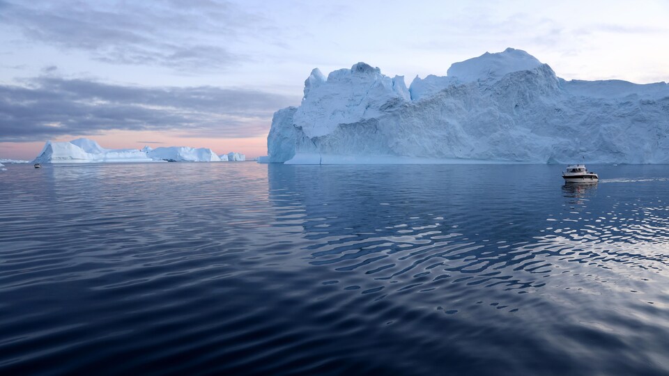 Un petit bateau navigue près d'icebergs au soleil couchant.